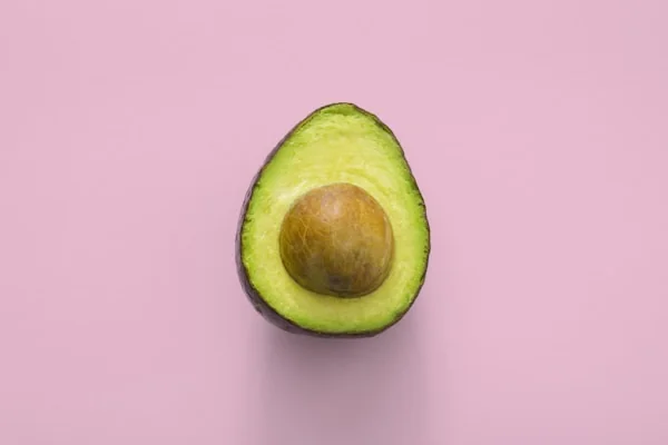 Aguacate abierto con el hueso y fondo color rosa